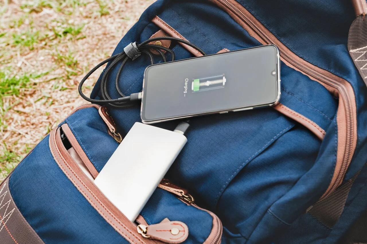 Powerbank ładujący telefon leżący na plecaku turystycznym na trawie